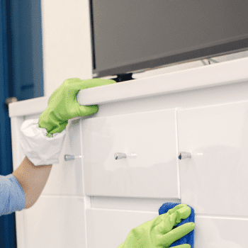 Una donna con guanti di gomma che pulisce il piano di lavoro della cucina con una spugna.